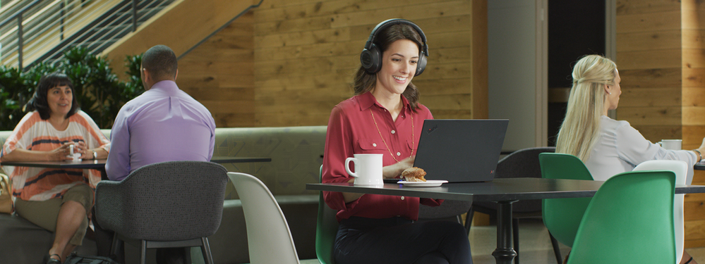 Person sitting in an open space environment wearing a Teams-certified headset while attending an online meeting