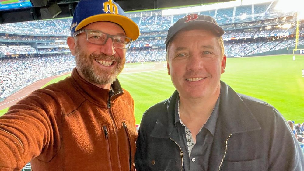 Mark Kashman (left) and Chris McNulty (right) taking in a Mariners game in Seattle, WA - wearing Mariners and Red Sox hats respectively.