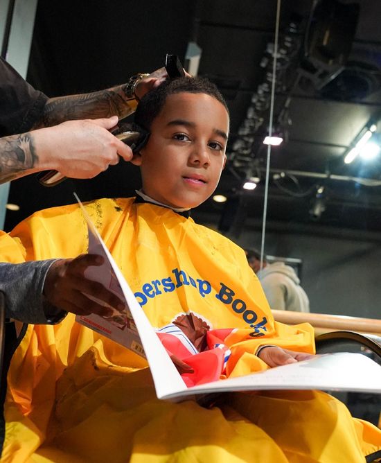 Young boy gets a haircut and reads a book at the Barbershop Books activation.