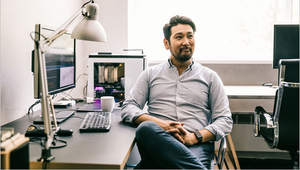 Smiling person sitting at a desk with computer and coffee cup