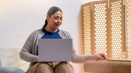 A woman seated in a stuffed chair works on a laptop.jpg