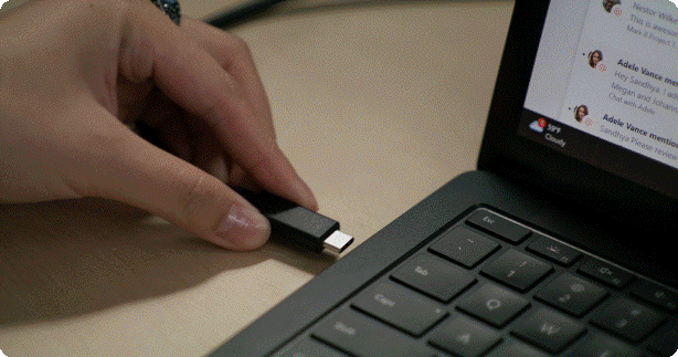 An individual plugs their laptop into a monitor and on-screen pop-ups confirm that their space has been reserved and that their workplace presence has updated to in-office.