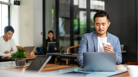 Three people sitting at different desks, working on laptops.