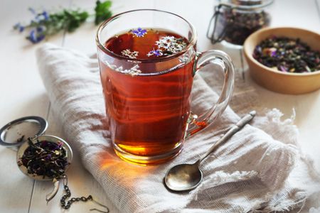 A cup of tea with purple flowers on a table with a tea cozy.