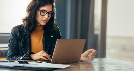 Person wearing glasses sitting at desk, looking intently at laptop screen