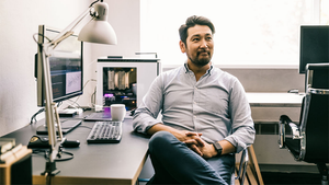 Man sitting casually at a desk with a desktop computer, keyboard, and coffee cup.