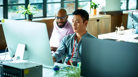 Two people sitting at desk in consultation while looking at a monitor.