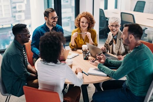 A photo of six people smiling and collaborating around a table.