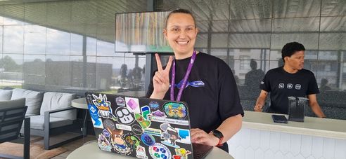 A woman smiling with her computer and pointing two fingers