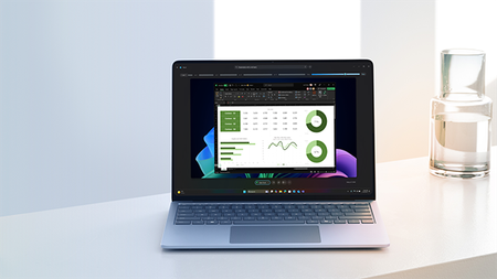 Copilot+ PC device on a desk with a pitcher of water beside it. On the screen, there is a shot of a Recall report with graphs and charts on dark background with Windows bloom.