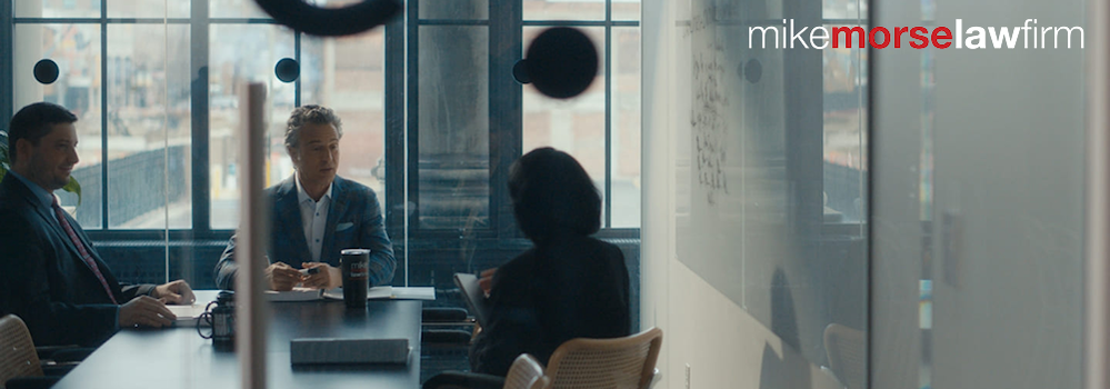 Photo representing Mike Morse Law Firm, showing three people sitting at a conference room table.