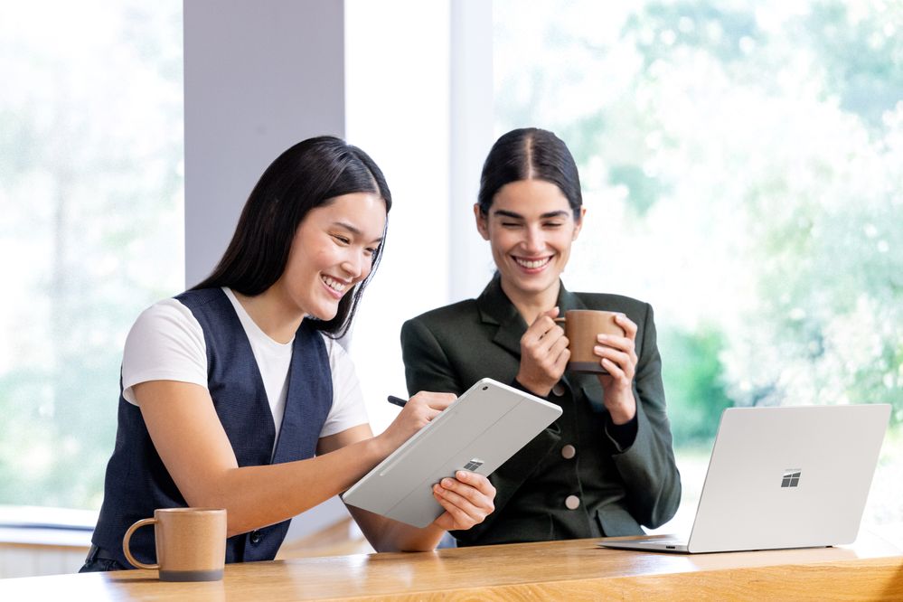 Two women smiling while looking at a Surface Pro 12-inch while one of them is writing on its screen