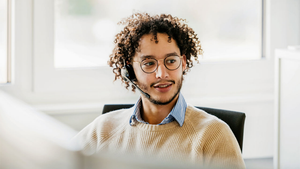 Person wearing a headset sits at a desk, looks toward something with interest