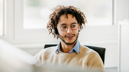 Person wearing a headset sits at a desk, looks toward something with interest