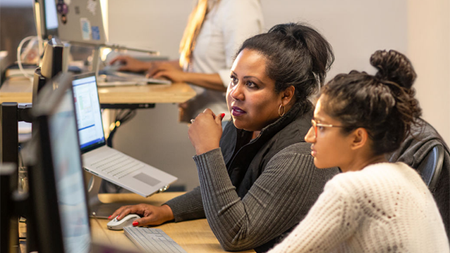 Two developers collaborating in front of laptops and monitors.