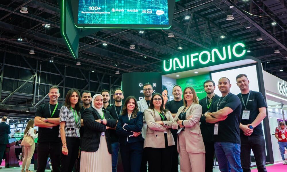 Photo of Unifonic employees standing in front of a neon Unifonic sign.