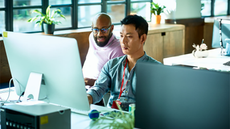 Two people in consultation sit at a desk while looking at a large monitor