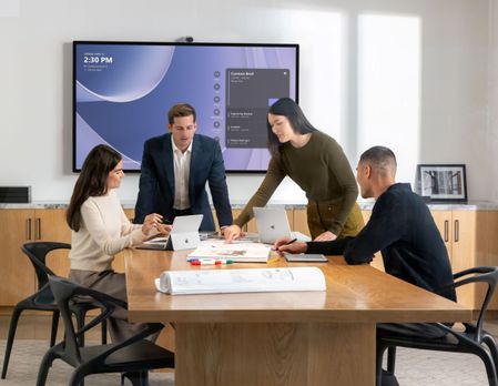 Photograph of four executives in a conference room. There is a Surface Hub mounted on the wall.