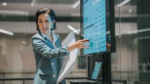 Businesswoman presents charts and graphs on a large display mirroring a laptop