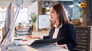 A woman in a pinstriped suit works on a desktop computer in an open office