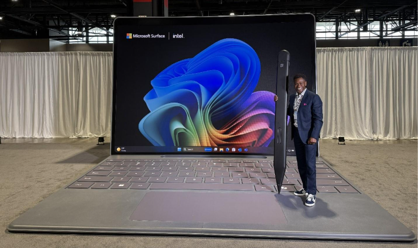 Man holding a giant pen while standing on a giant model of a Surface Pro