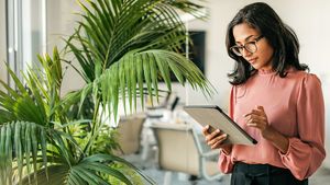 a-woman-standing-using-a-tablet-beside-a-large-plant-in-a-modern-office.