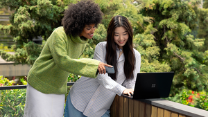 Two women stand outside using a Surface Laptop and a mobile device