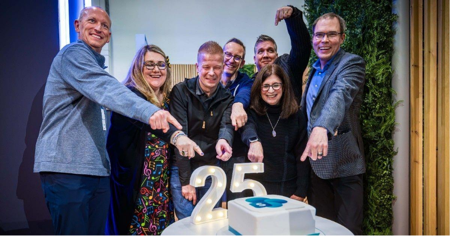 Picture of community members gathered around a 25th birthday cake for SharePoint