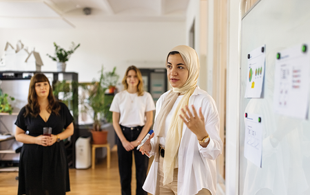 A businesswoman standing in front of a whiteboard gives a presentation to colleagues