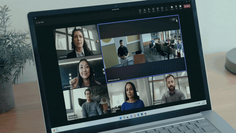 A gif of a laptop, with a Teams meeting on screen switching between multiple different camera angles of attendees in a Teams room.