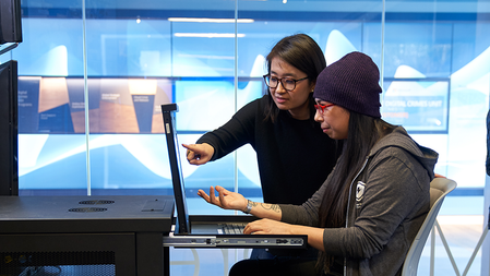 Two women, one seated and the other standing, work at a server console cart