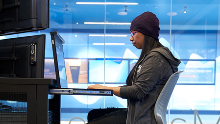 Woman wearing knit hat, glasses and hoodie sits working at a server terminal cart