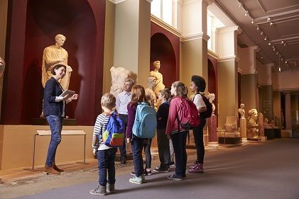 Teacher and kids with backpacks in a sculpture gallery in a museum